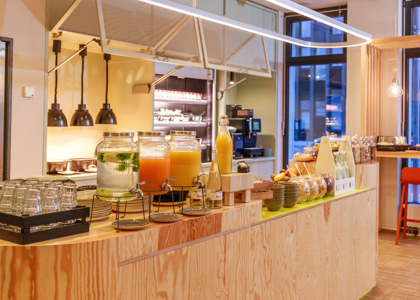 Frühstücksbuffet mit Getränkespendern, Gläsern und Obst in heller Küche mit freundlicher Holzverkleidung.