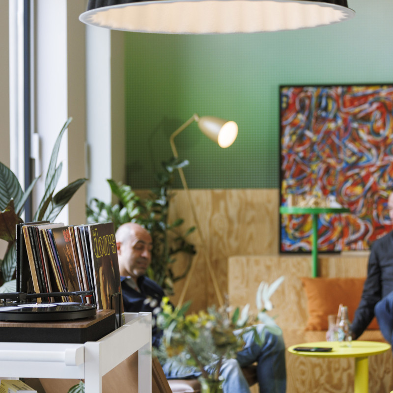 Gemütliche Hotellounge mit vielen Pflanzen, einem Schallplattenspieler und Gästen, die entspannen.