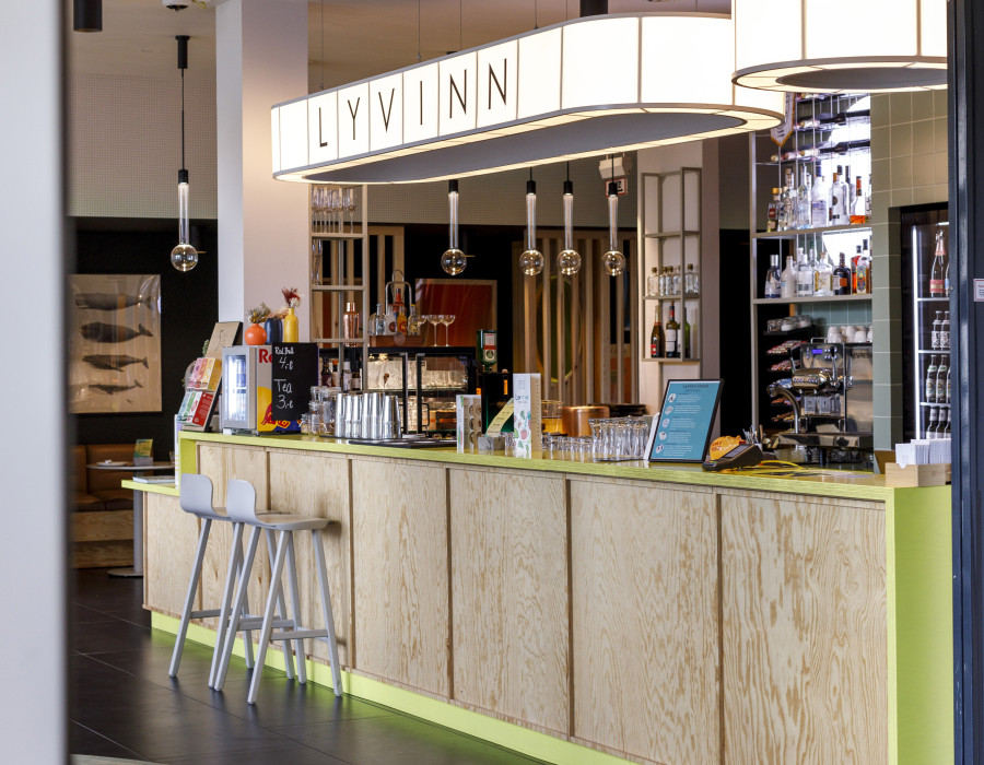 Moderne Hotelbar mit hellem Holzdesign, Neonakzenten und gemütlicher Atmosphäre im LYV INN.