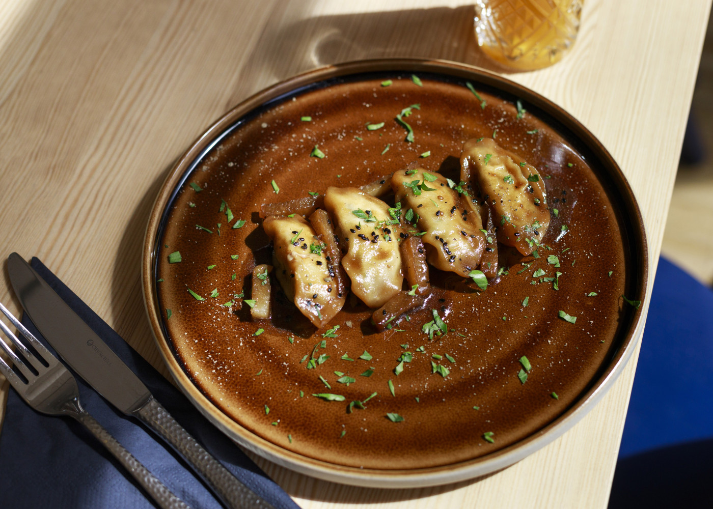 Fünf goldbraun gebratene Gyoza auf einem braunen Teller, garniert mit gehackten Kräutern auf hellem Tisch.