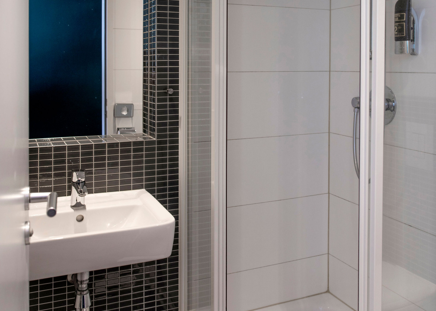 Kompaktes, modernes Badezimmer mit weißer Dusche, Waschbecken, Spiegel und dunkler Fliesenwand.