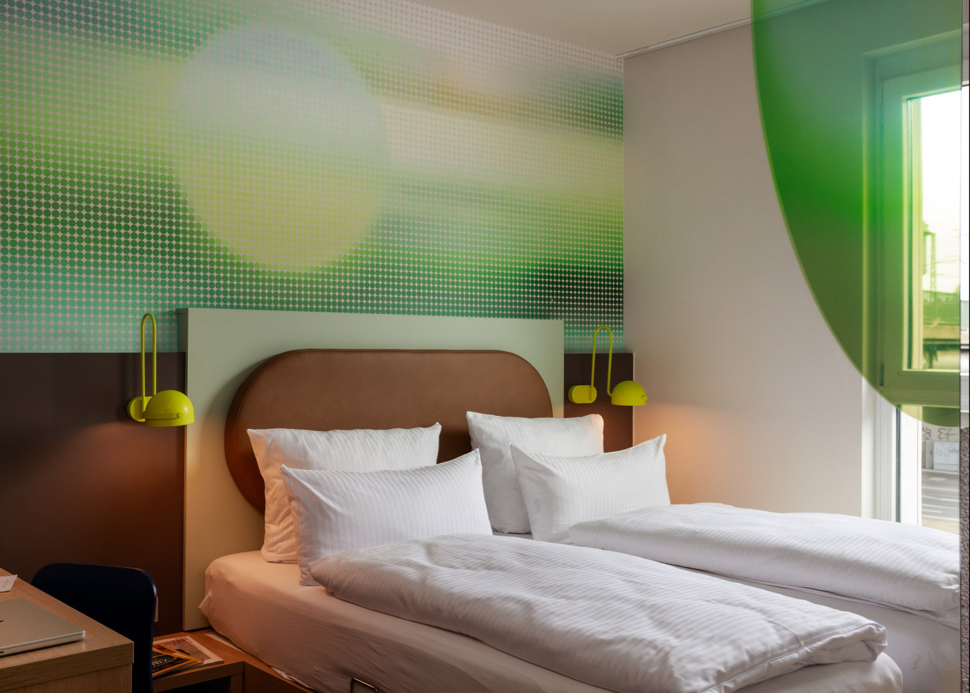 Modernes Hotelzimmer mit großem Doppelbett, abstrakter grüner Wandgestaltung und natürlichem Tageslicht.