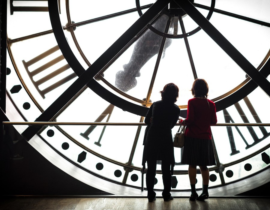 Zwei kleine Kinder stehen hinter einer Uhr eines Museums.