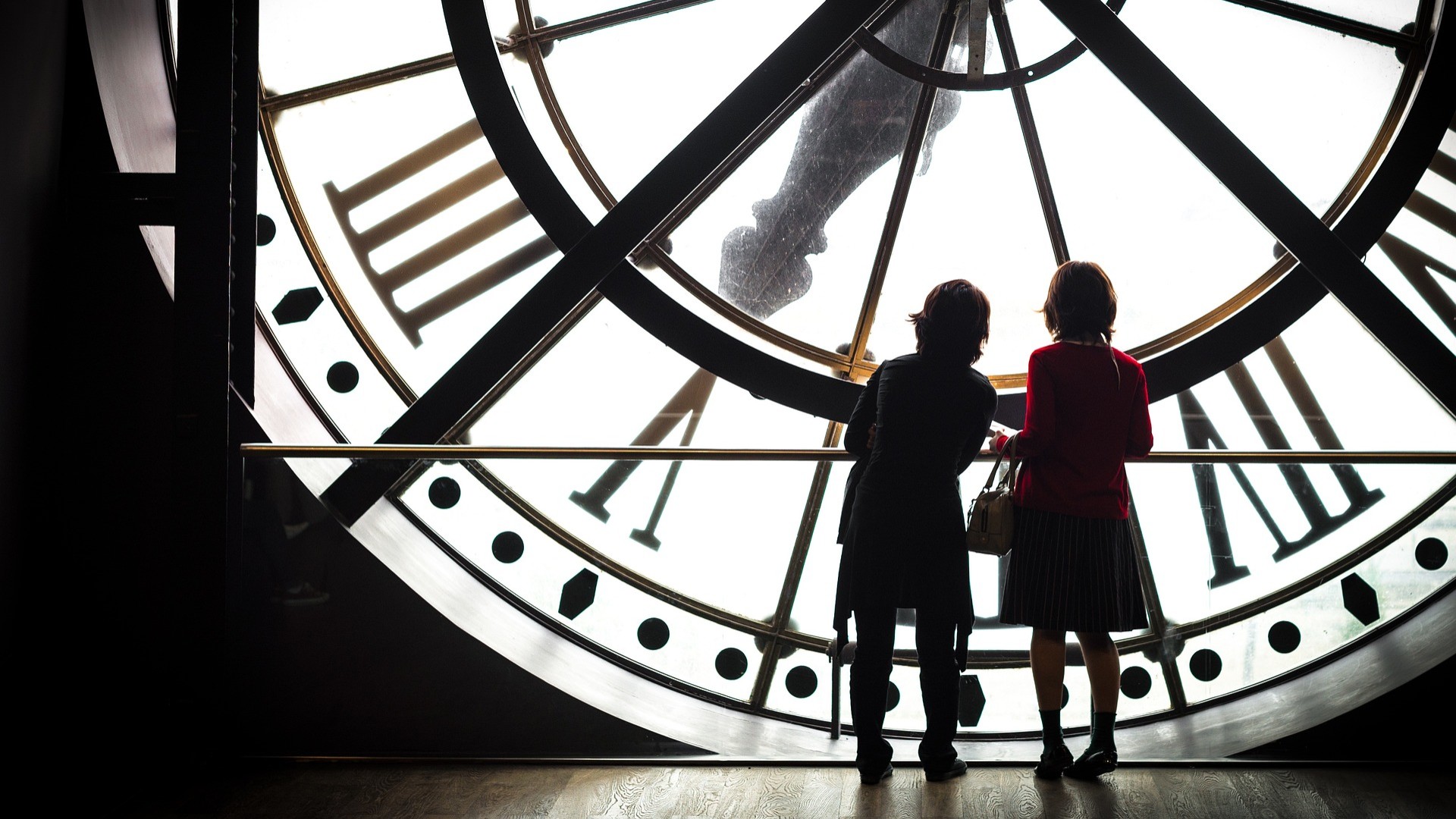 Zwei Kinder stehen hinter einer großen Uhr eines Museums.