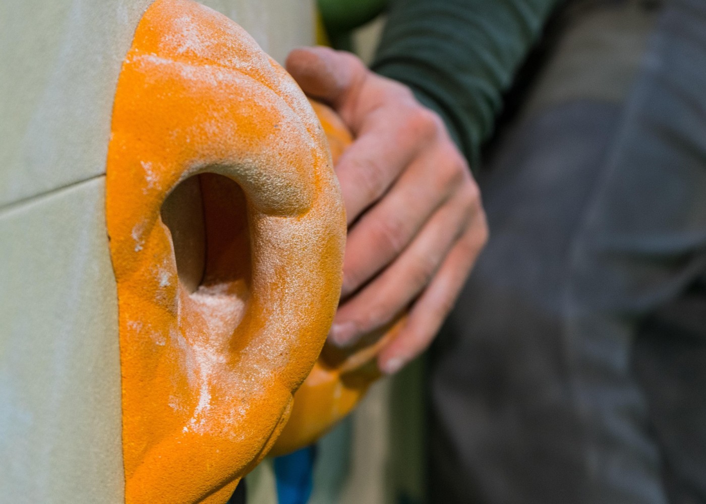 Nahaufnahme einer Hand, die einen orangefarbenen Klettergriff an einer Kletterwand festhält.