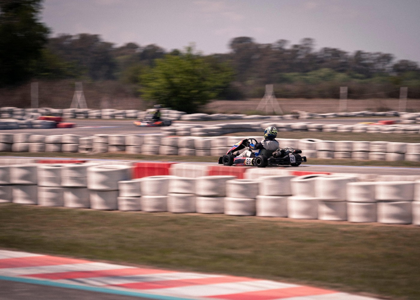 Fahrer in Go-Karts auf einer Outdoor-Kartbahn, umgeben von weißen Reifenbarrieren, bei einem spannenden Rennen auf der Strecke.