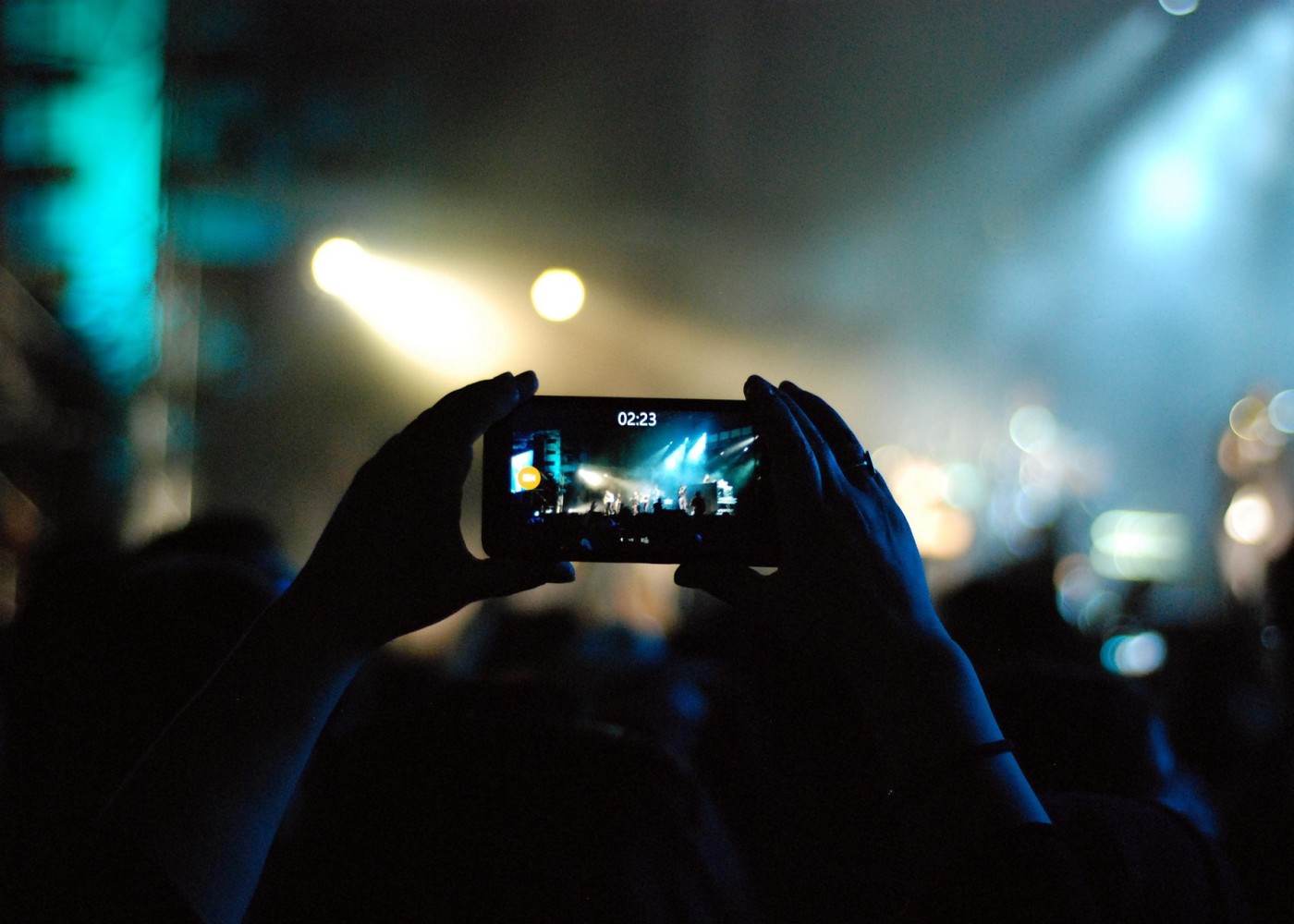 Blick auf zwei Hände, die ein Handy halten, dass ein Konzert filmt.