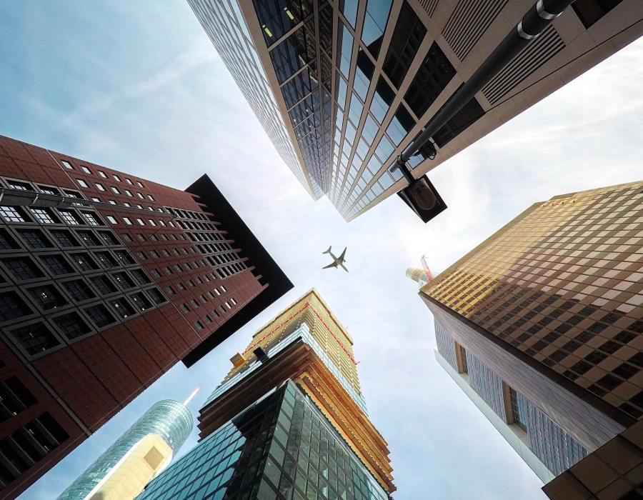 Perspektive nach oben zwischen Hochhäusern in der Stadt mit Flugzeug, das mittig durch den Himmel fliegt.